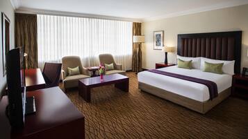 Habitación de hotel con una cama grande, dos sillones, una mesa de centro, un televisor y un escritorio.
