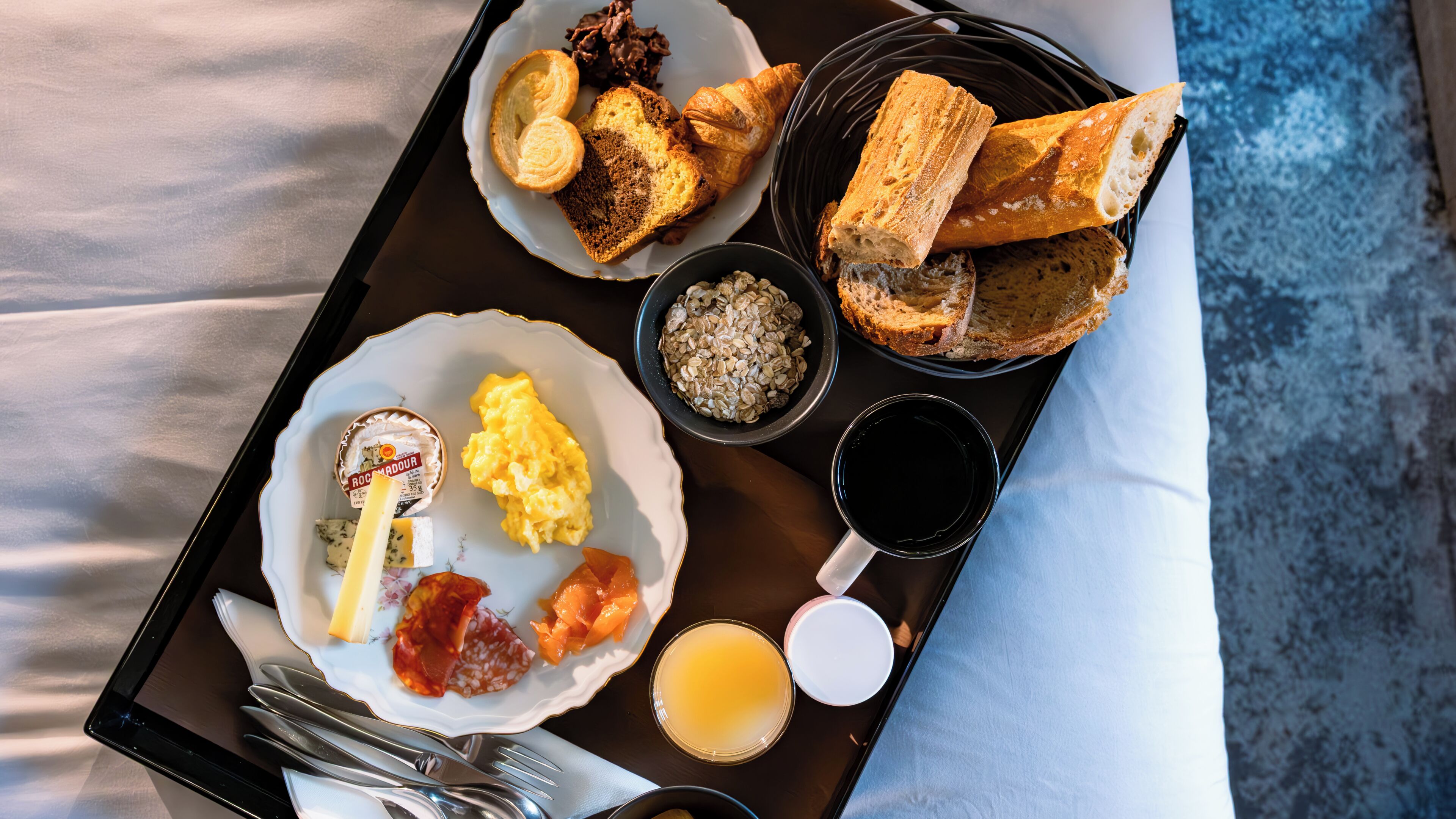 Una bandeja con alimentos para el desayuno, incluyendo cruasanes, huevos revueltos y un tazón de avena.