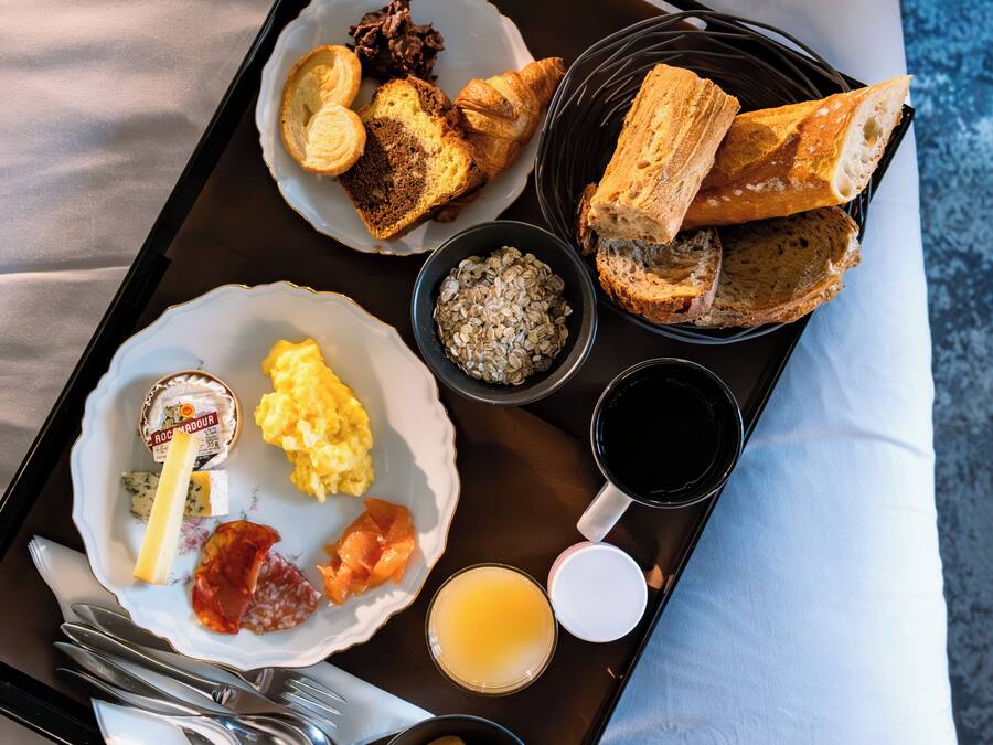 Una bandeja con alimentos para el desayuno, incluyendo cruasanes, huevos revueltos y un tazón de avena.