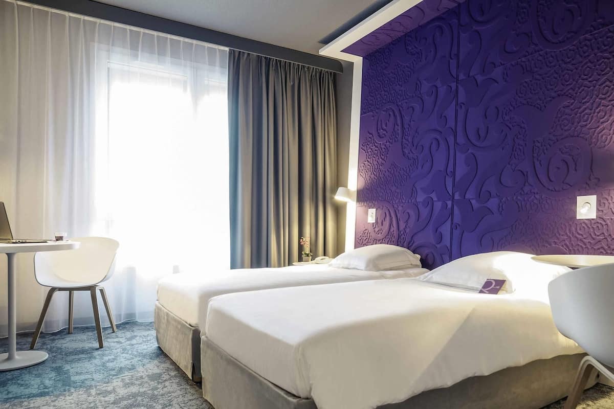 Quarto de hotel com duas camas, uma escrivaninha e uma cadeira.