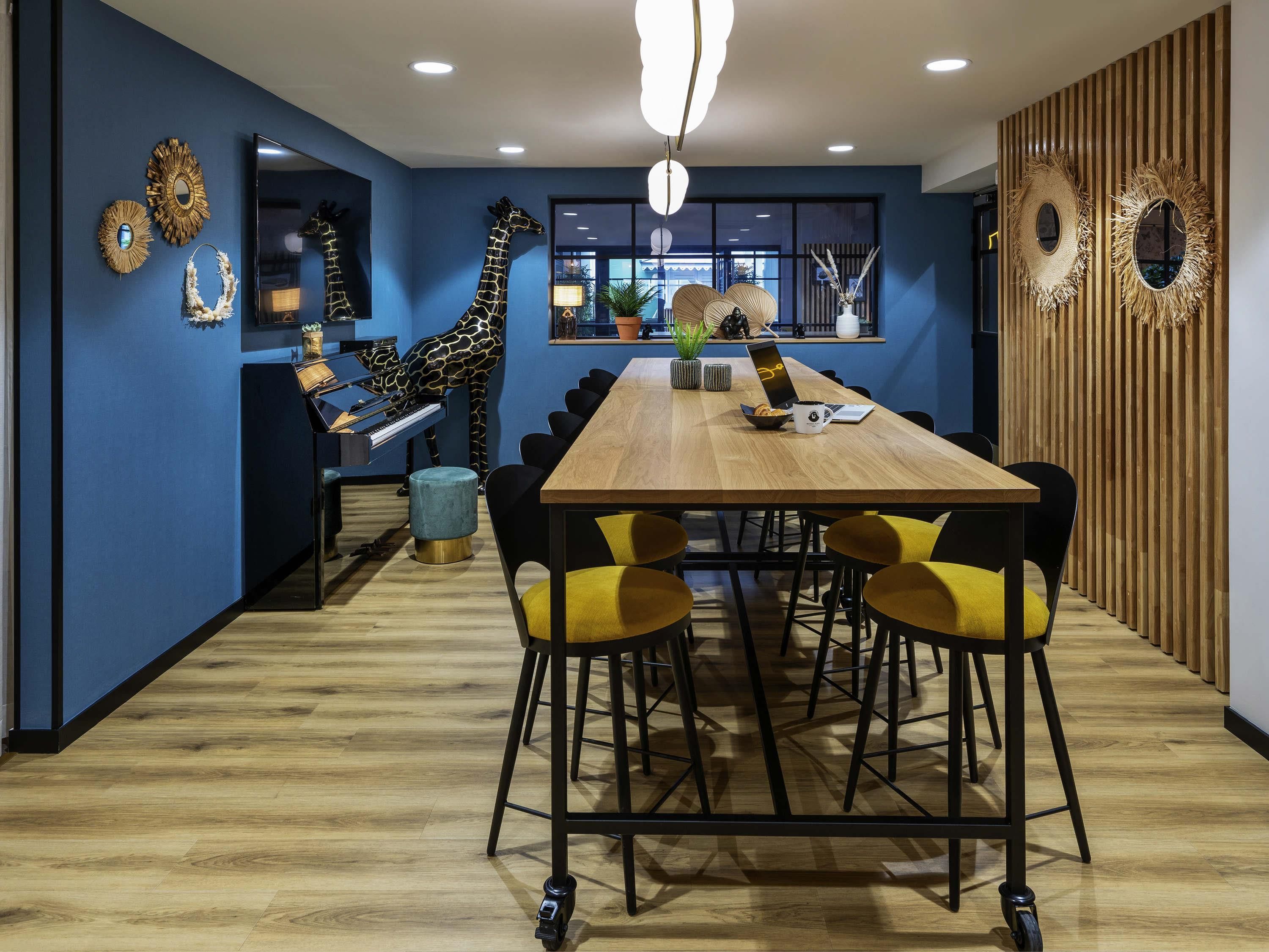A modern dining area with a long wooden table, yellow chairs, and a giraffe sculpture.