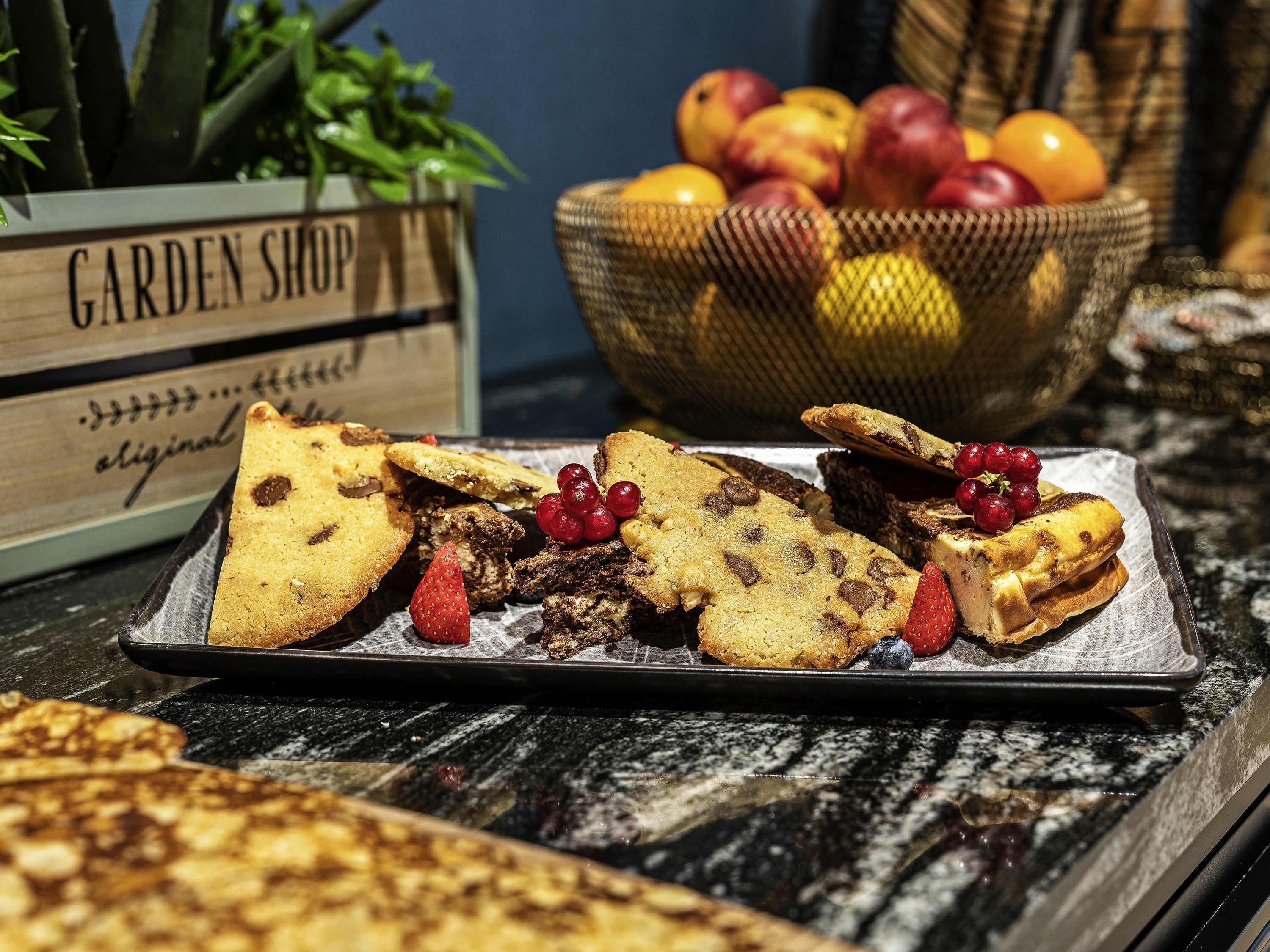 A tray of assorted baked goods with berries and a basket of fruits in the background.
