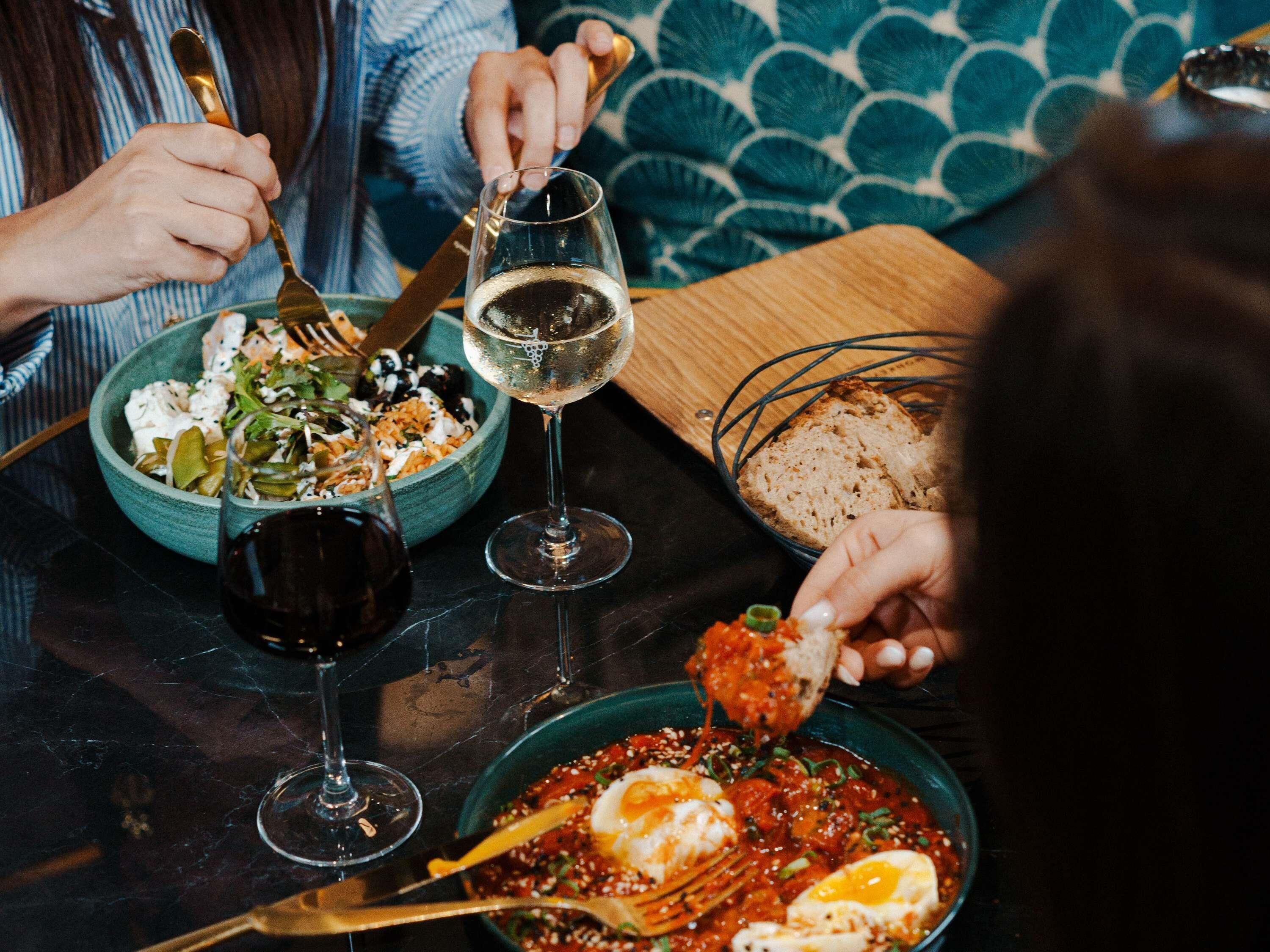 A dining table with a salad, a bowl of soup, and a plate with eggs and sauce. There are wine glasses and cutlery on the table.