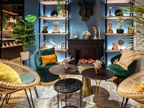 Una sala de estar acogedora con chimenea, sillones verdes y una variedad de objetos decorativos en estantes.