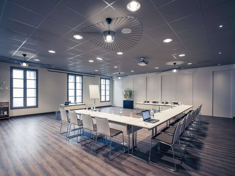 Un salón de conferencias con una larga mesa, sillas, una pizarra y una planta en maceta.