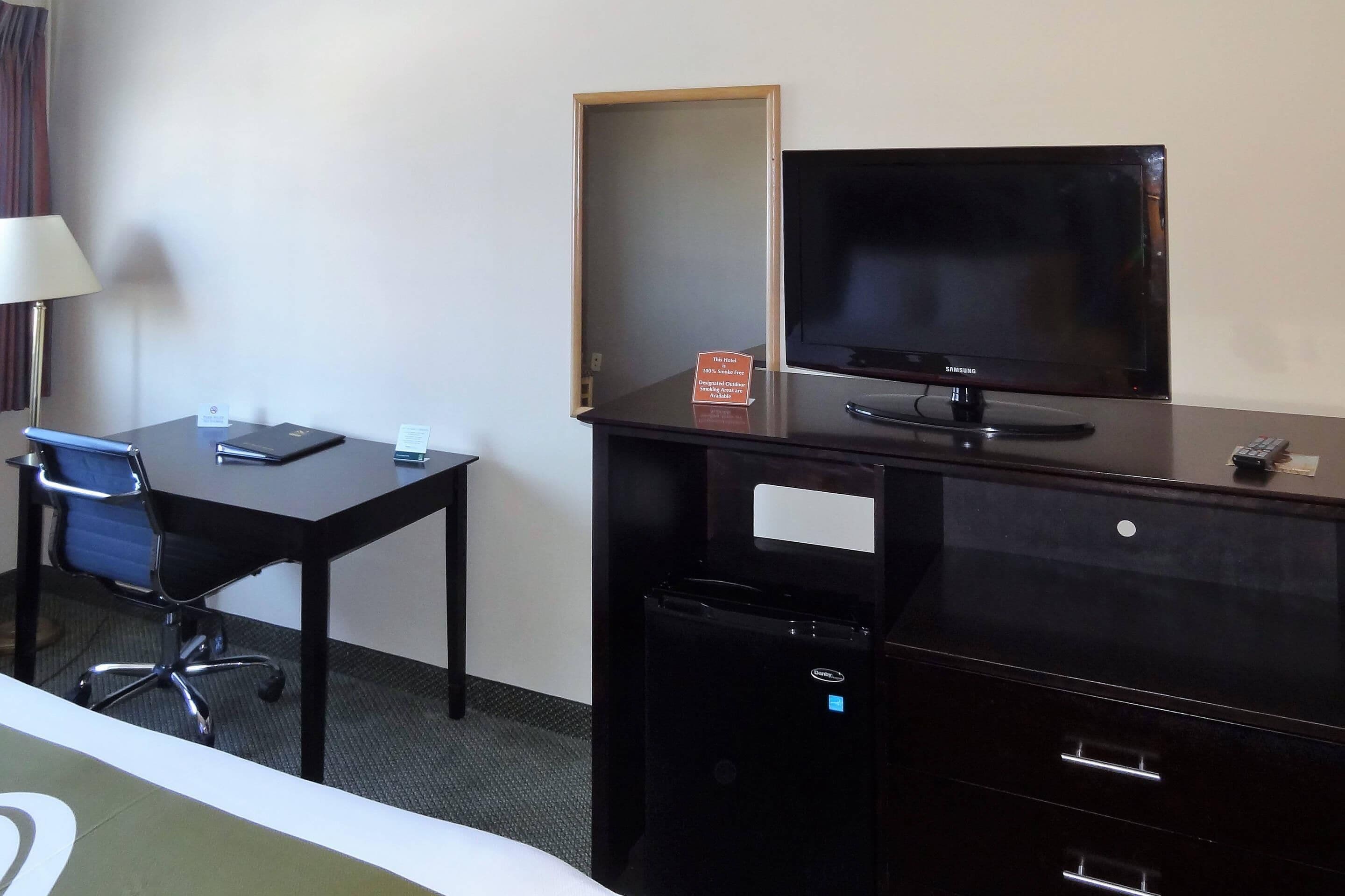 A hotel room with a desk, chair, television, and a trash bin.