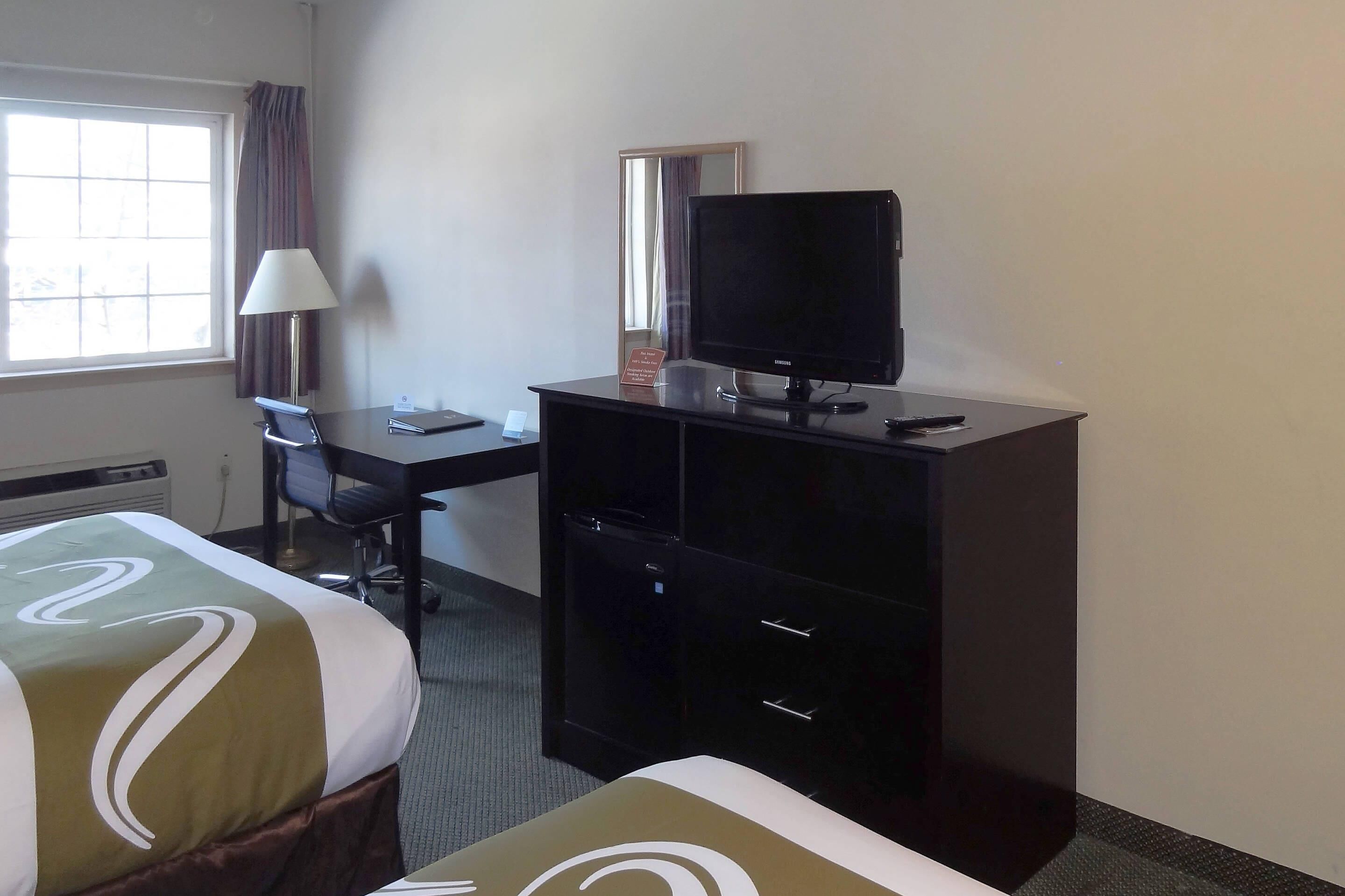 A hotel room with a bed, a desk with a computer, a television, and a window with curtains.