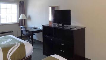 A hotel room with a bed, a desk with a computer, a television, and a window with curtains.