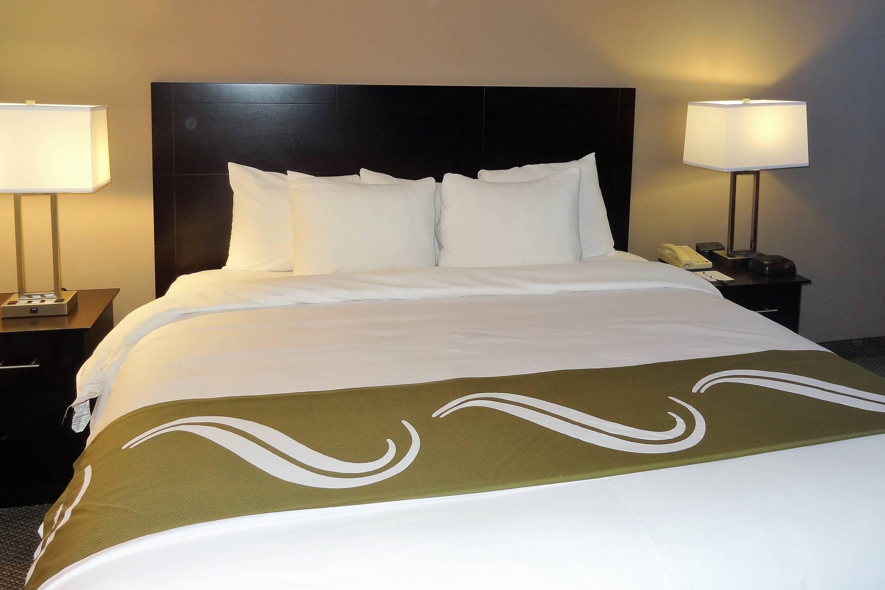 Habitación de hotel con una cama grande, dos mesitas de noche y una lámpara a cada lado.