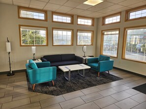 Une pièce avec un canapé foncé, deux fauteuils turquoise, une petite table blanche et un lampadaire.