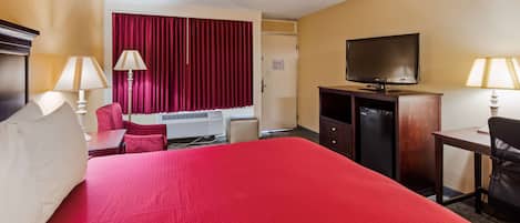 Habitación de hotel con una cama grande, un escritorio, una silla, televisión y un minibar.