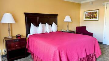 Habitación de hotel con una cama grande, dos mesitas de noche, una silla, una lámpara y un cuadro en la pared.