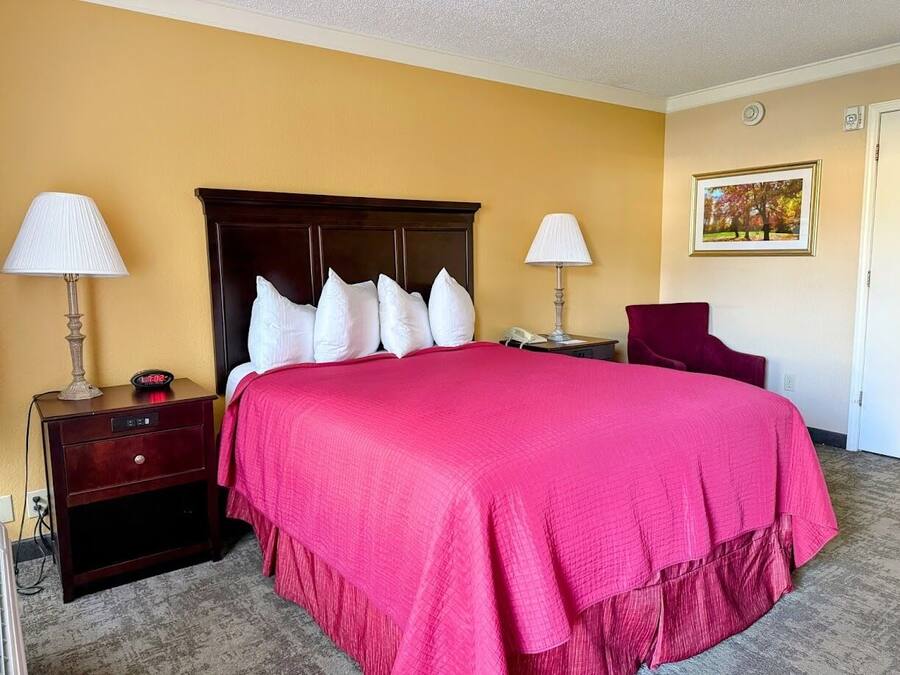 A hotel room with a large bed, two bedside tables, a chair, a lamp, and a painting on the wall.