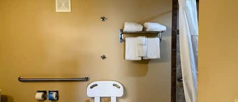A small, compact bathroom with a toilet, a raised toilet seat, a handrail, a towel rack with towels, and a shower curtain.