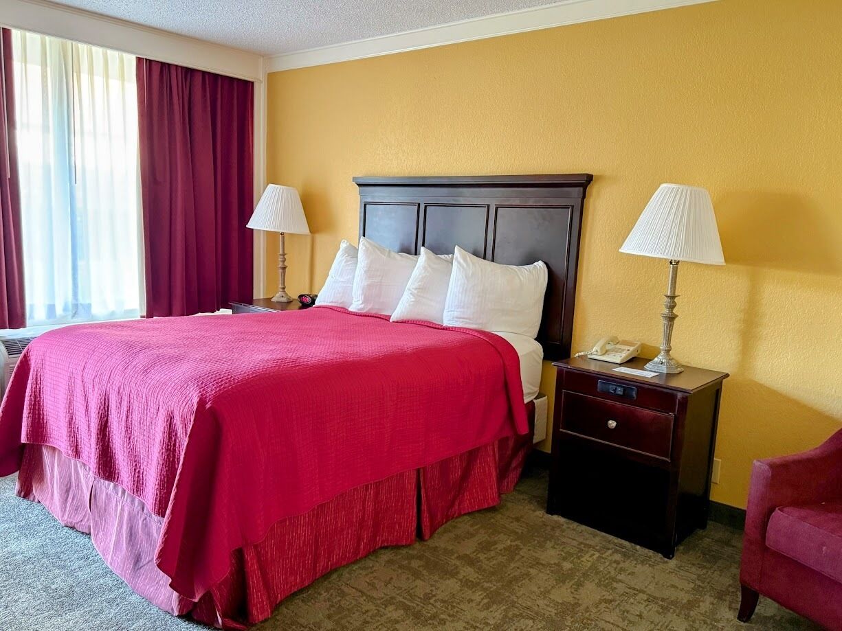 A hotel room with a large bed, two bedside tables, a nightstand, a red chair, and a window with curtains.