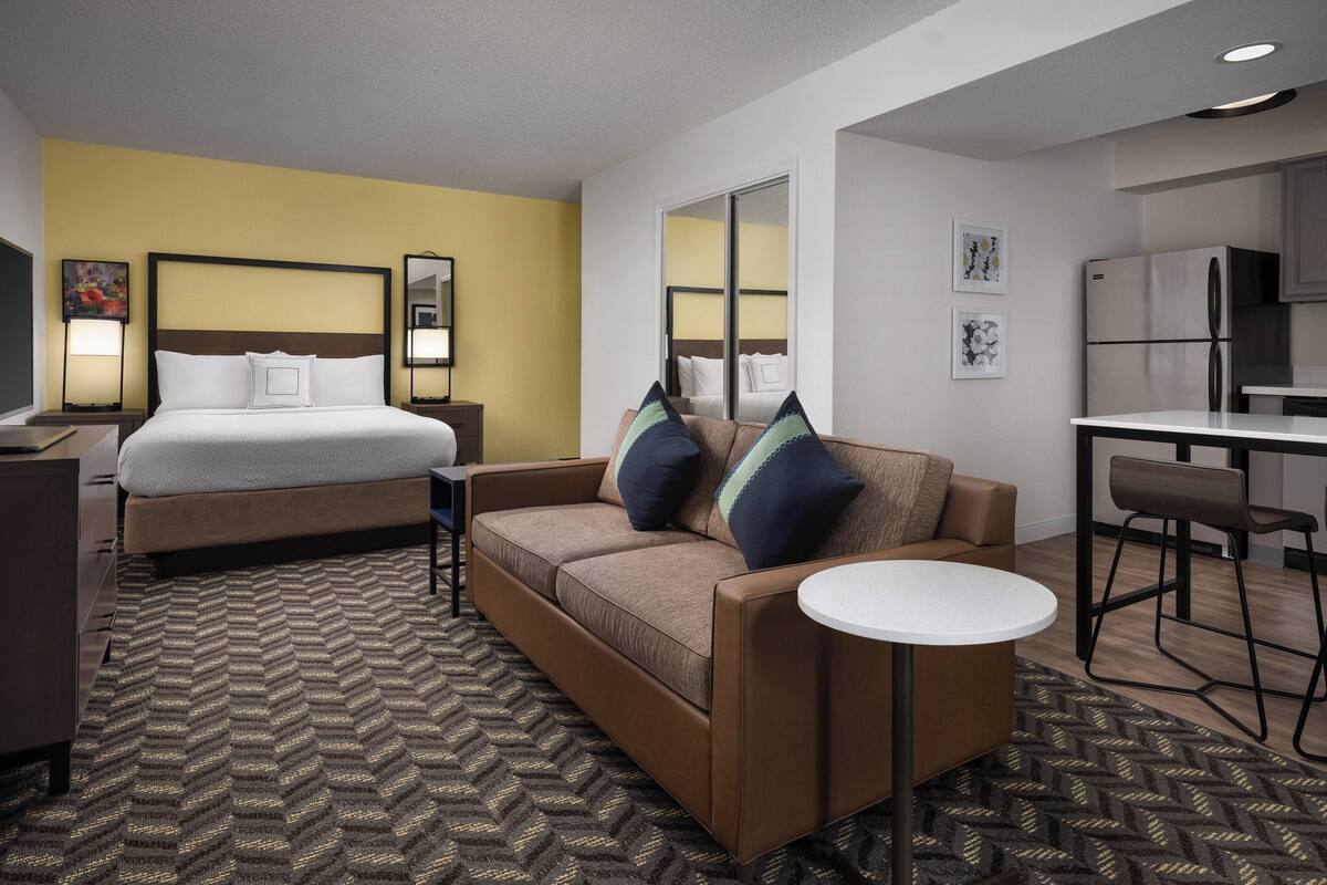 Une chambre d’hôtel comprenant un lit, un canapé, une petite table, un bureau et un coin cuisine.