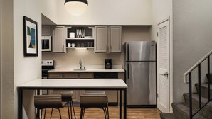 A compact kitchen with a central island, stainless steel appliances, and a staircase leading to an upper level.