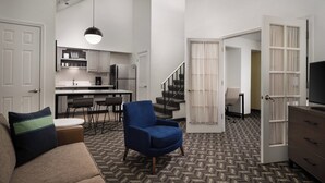 A modern living room with a sofa, armchair, and a dining area with a kitchen in the background.