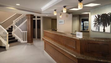 Zona de recepción de hotel con mostrador de madera, una escalera con barandas blancas y un cartel que indica 'Marriott Bonvoy'.