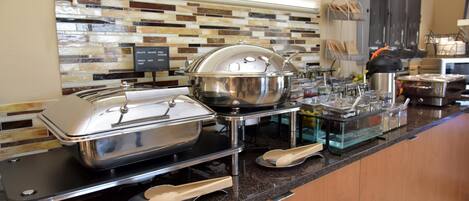 A buffet setup with various food containers and serving utensils.