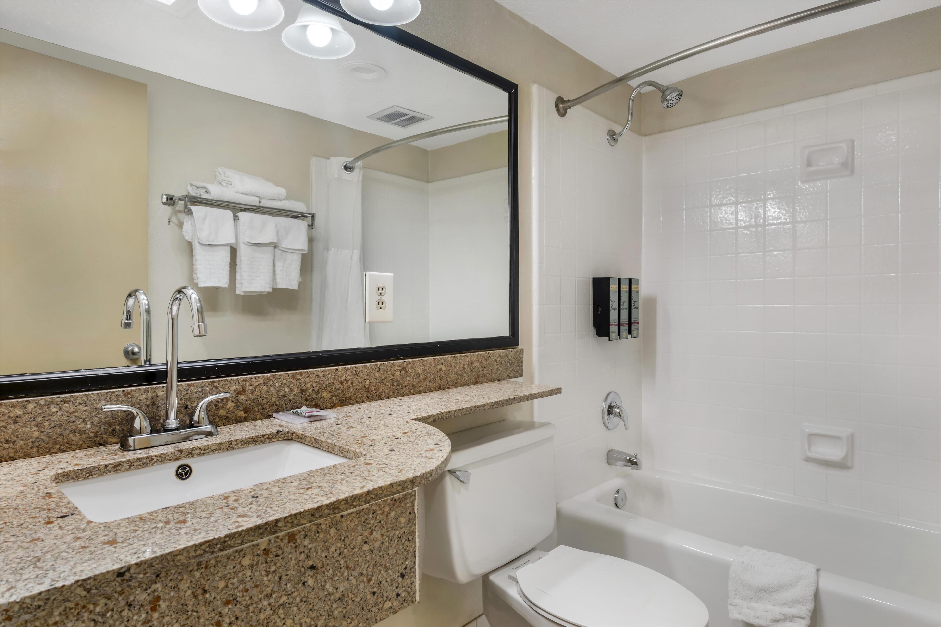 A modern bathroom with a granite countertop sink, a large mirror, a shower, and a toilet.