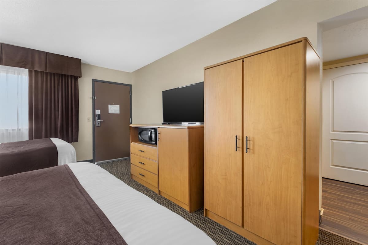 A hotel room with two beds, a wooden wardrobe, a television, and a microwave.