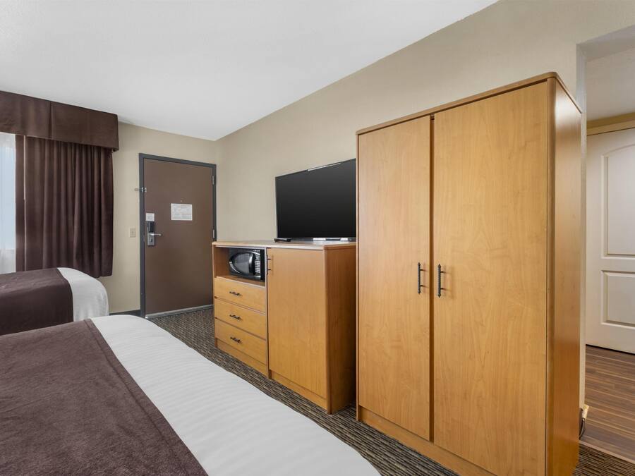 Una habitación de hotel con dos camas, un armario de madera, un televisor y un microondas.