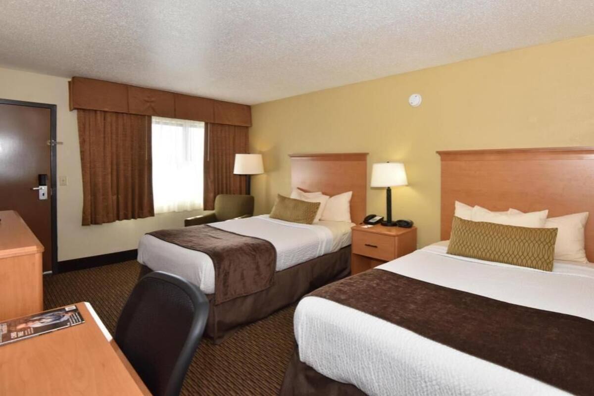 A hotel room with two beds, a desk, and a chair.