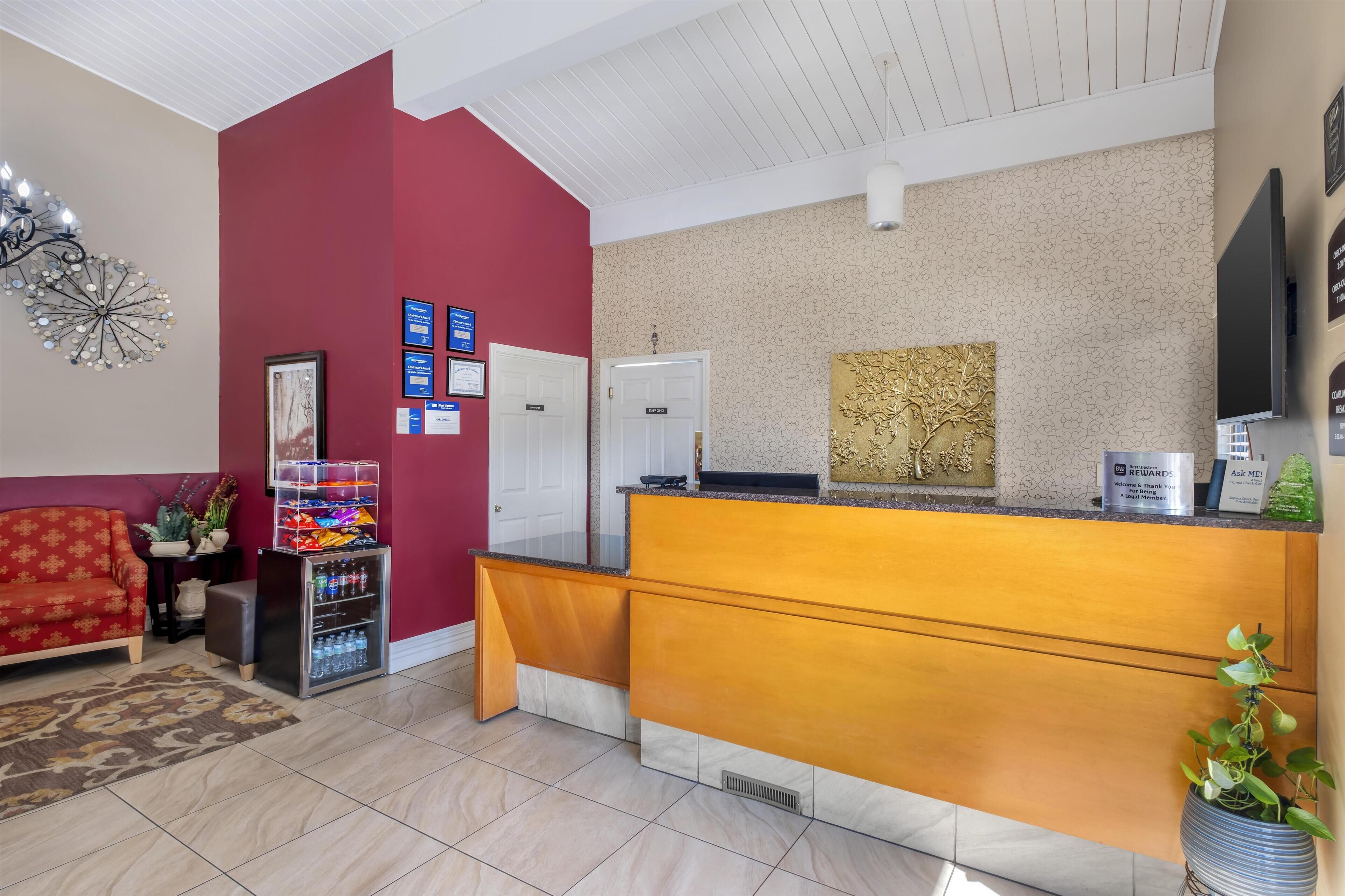 A reception area with a wooden counter, a red wall, a chandelier, and a television.