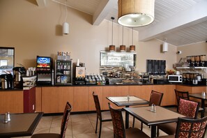 Un restaurante con mostrador, mesas, sillas y una zona de cocina con electrodomésticos y alimentos.