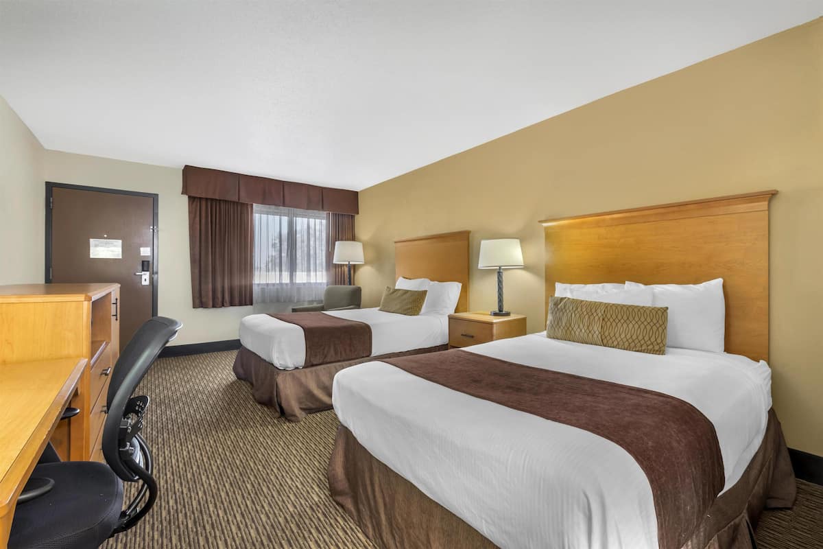 A hotel room with two beds, a desk, and a chair.