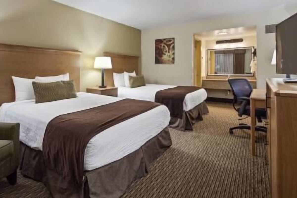A hotel room with two beds, a desk, a chair, and a television.