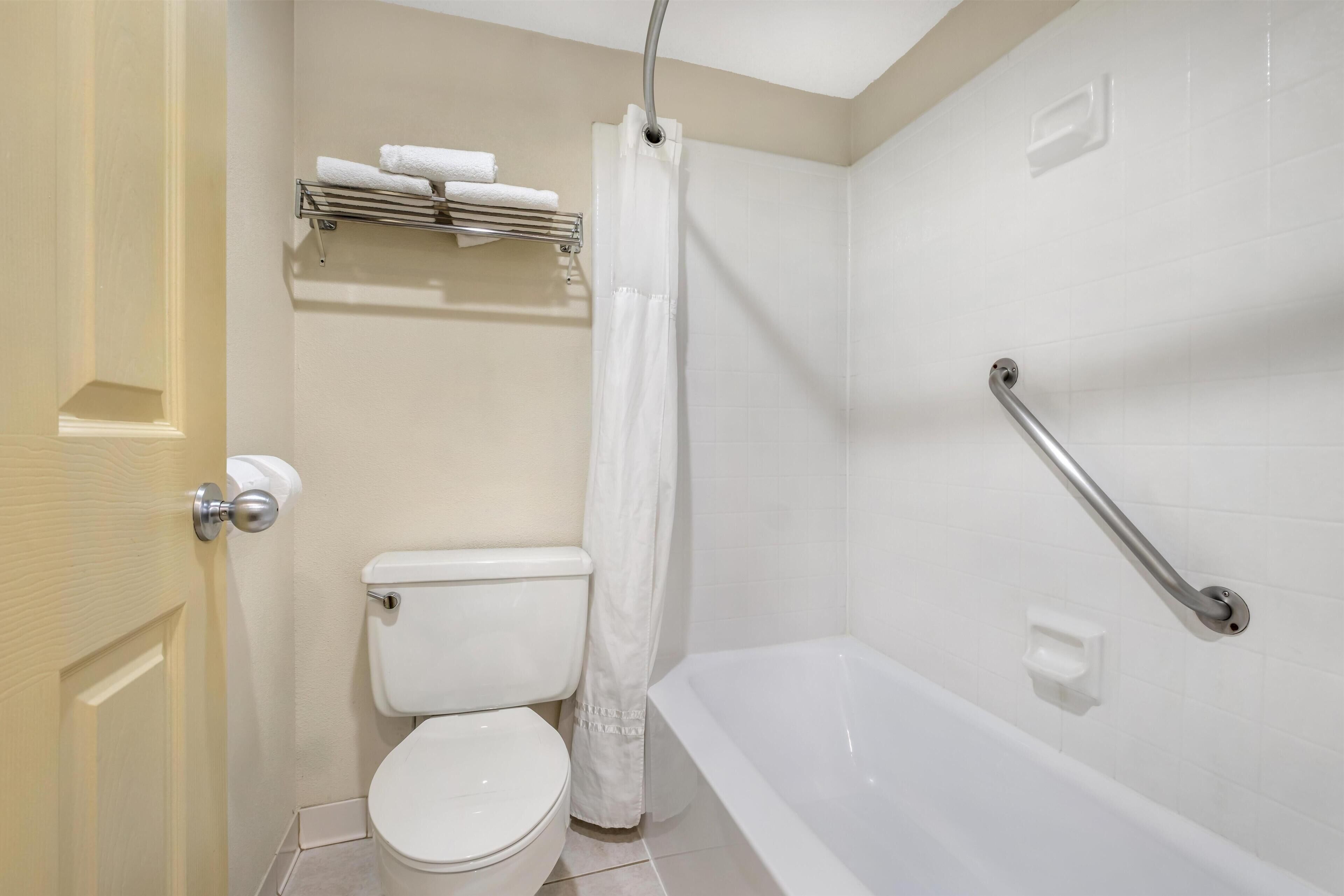 A bathroom with a toilet, a shower with a curtain, and a grab bar.