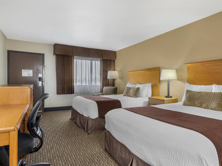 A hotel room with two beds, a desk, and a chair.