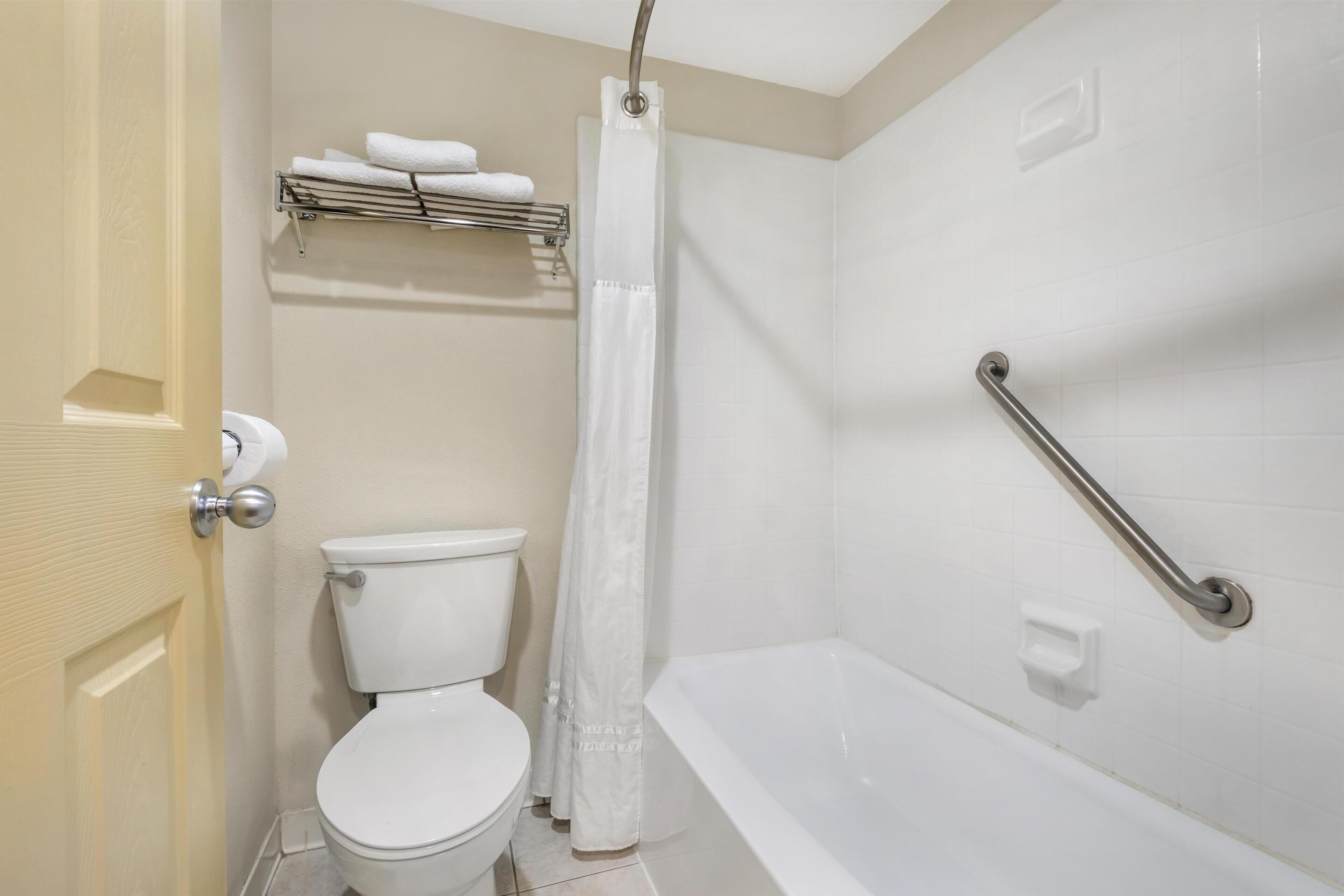 A bathroom with a toilet, a shower with a curtain, a bathtub with a grab bar, and a towel rack with towels.
