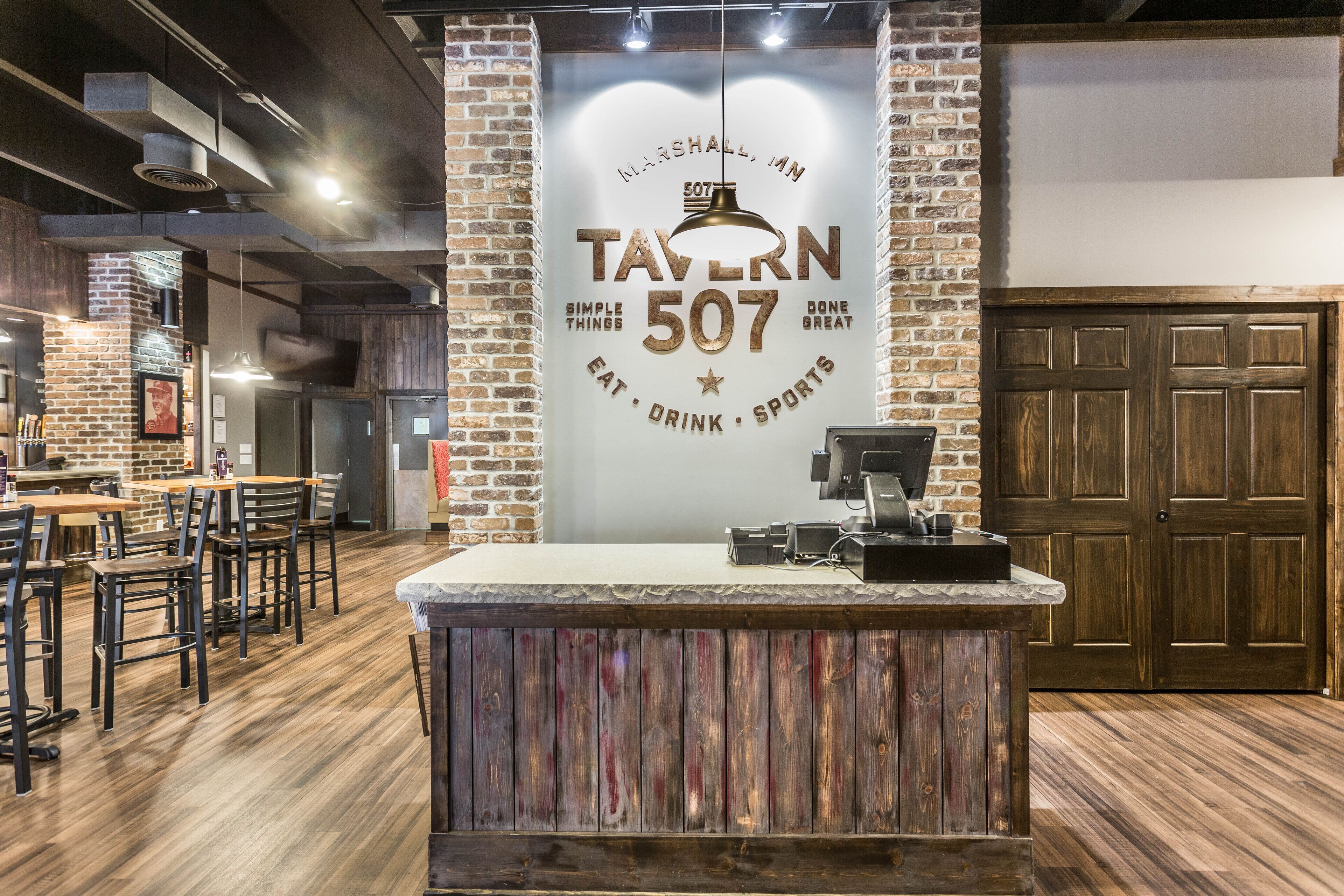 A restaurant interior with a brick wall, wooden flooring, and a counter with a menu display.