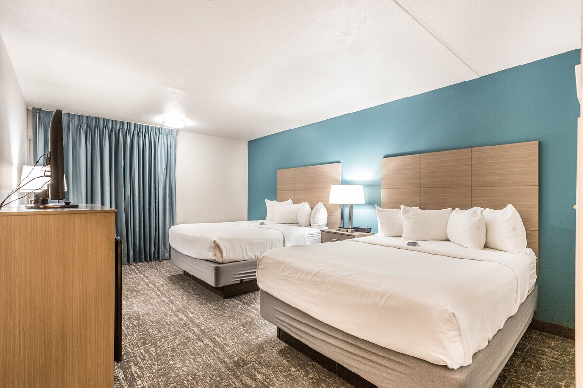 A hotel room with two beds, a desk, and a lamp.