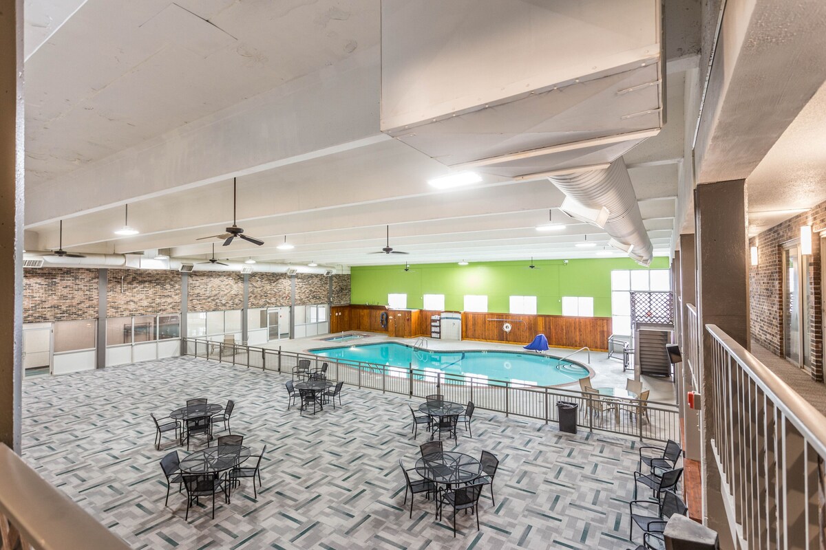A spacious indoor pool area with multiple seating arrangements and a green wall in the background.