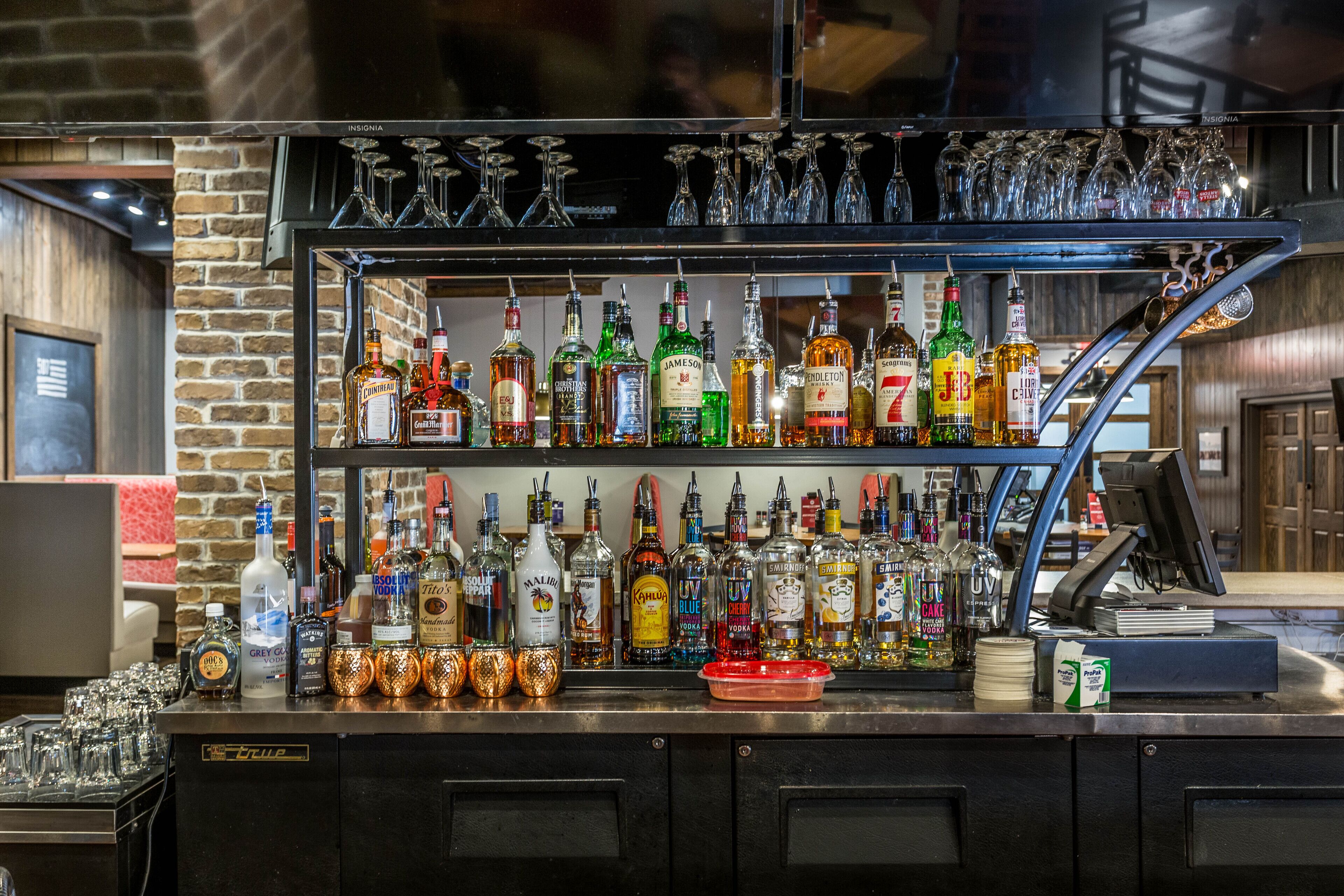 Una zona de bar con varias estanterías llenas de botellas de licores, vasos y una caja registradora.