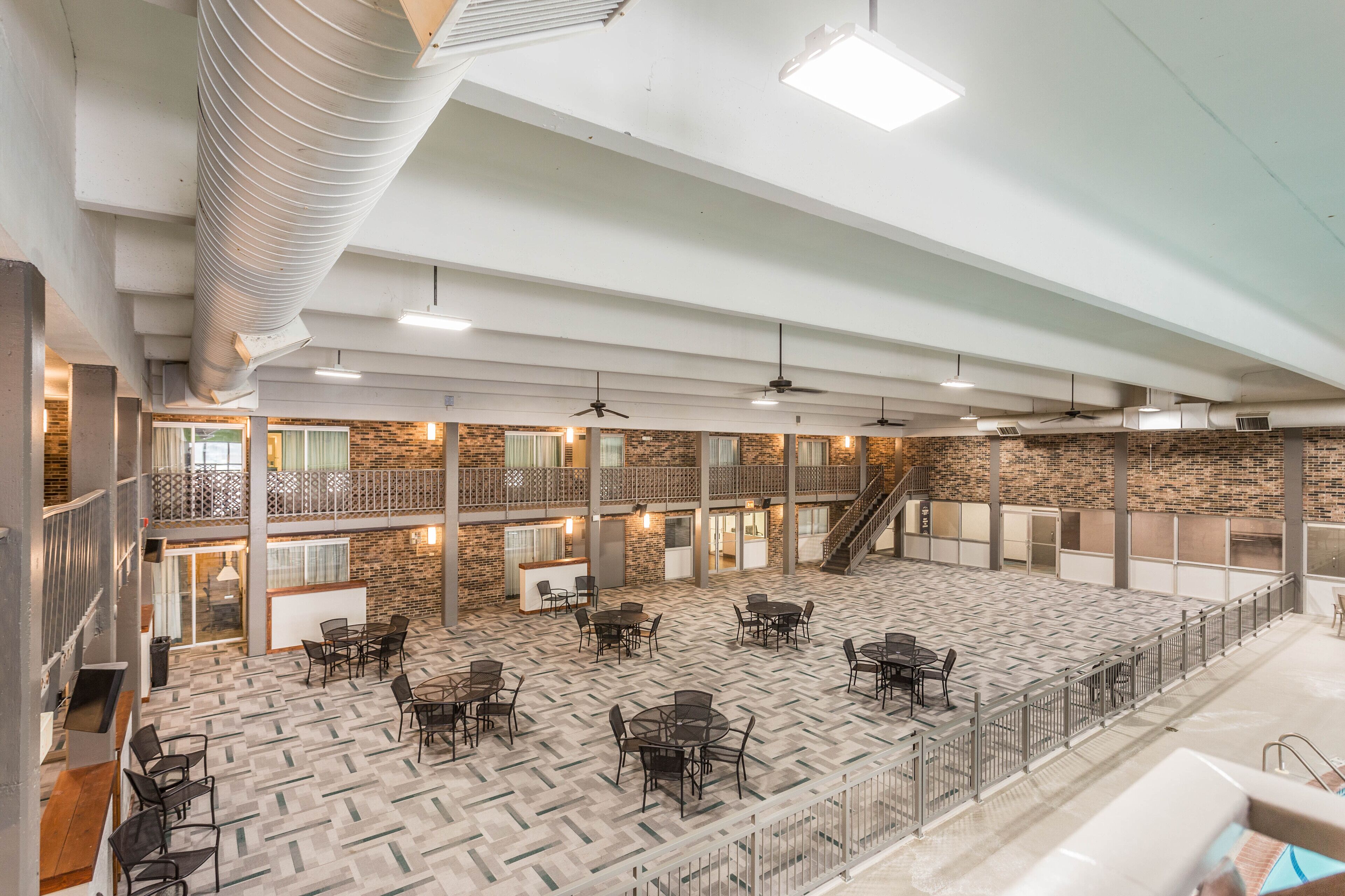 A spacious indoor area with multiple tables and chairs, a staircase, and a mix of brick and concrete flooring.