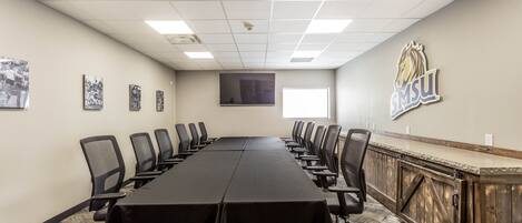 A conference room with a long table, chairs, a wooden cabinet, and a mounted television.