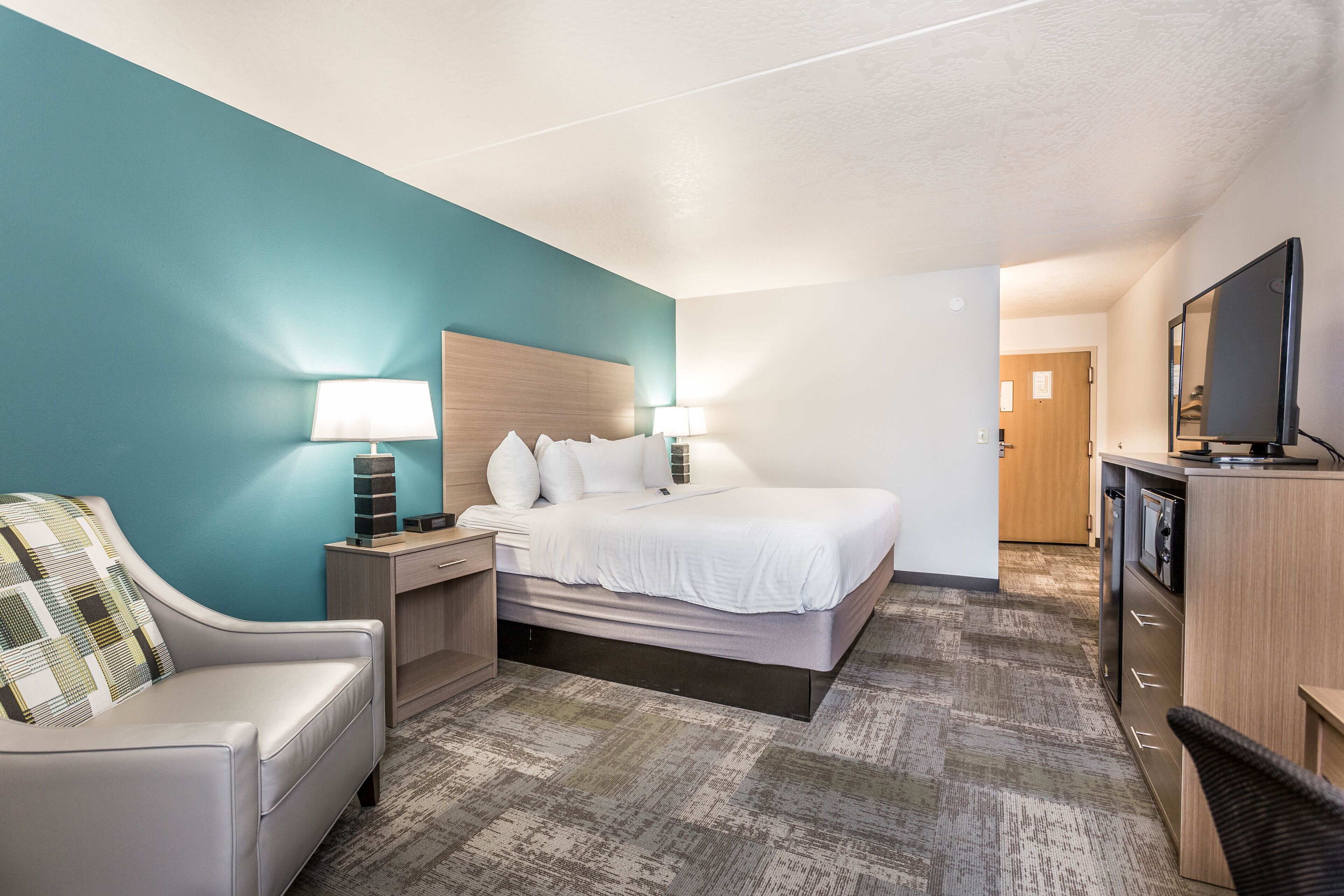 A hotel room with a bed, a desk, a chair, a TV, and a door leading to another room.