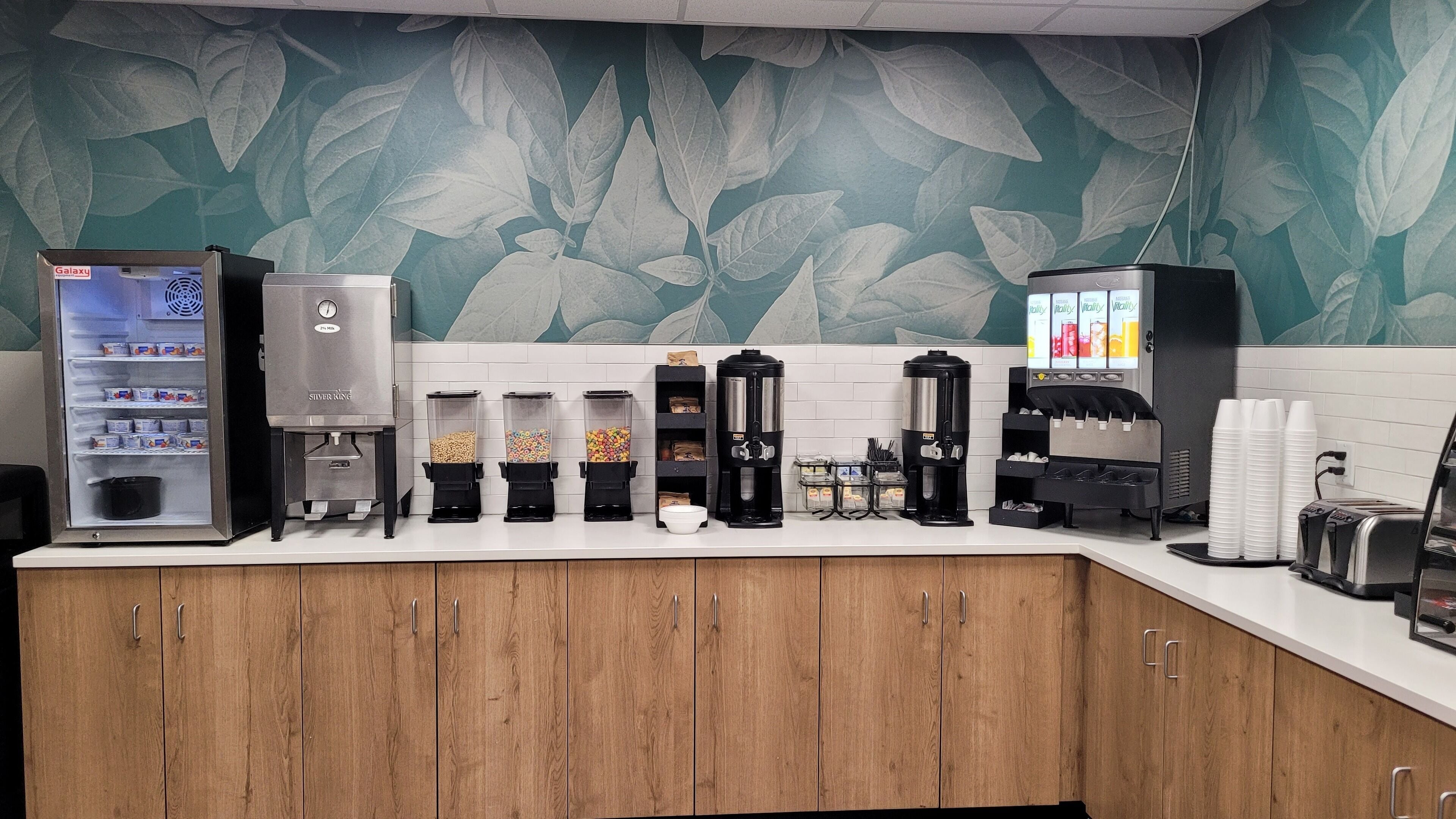 A self-service beverage station with various dispensers, a refrigerator, and a coffee machine.