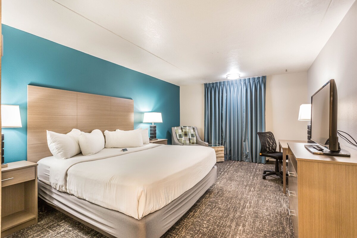 A hotel room with a large bed, a desk with a computer, a chair, a lamp, and a TV.