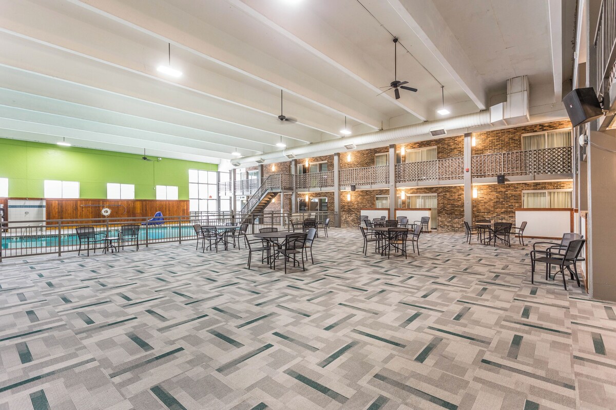 A spacious indoor area with a pool, multiple dining tables, and a staircase leading to an upper level.