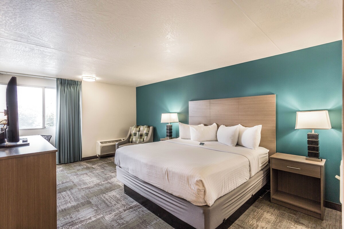 A hotel room with a large bed, two bedside tables with lamps, a desk with a television, and a window with curtains.