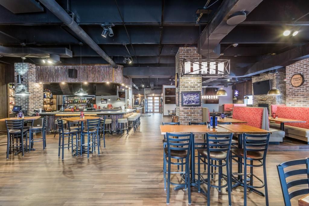 En rummelig restaurant med højt til loftet, synlige ventilationsrør og både bar- og spiseområder.
