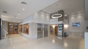 Un hall d’entrée spacieux avec un plafond haut, un ascenseur central et un escalier menant à un autre étage.