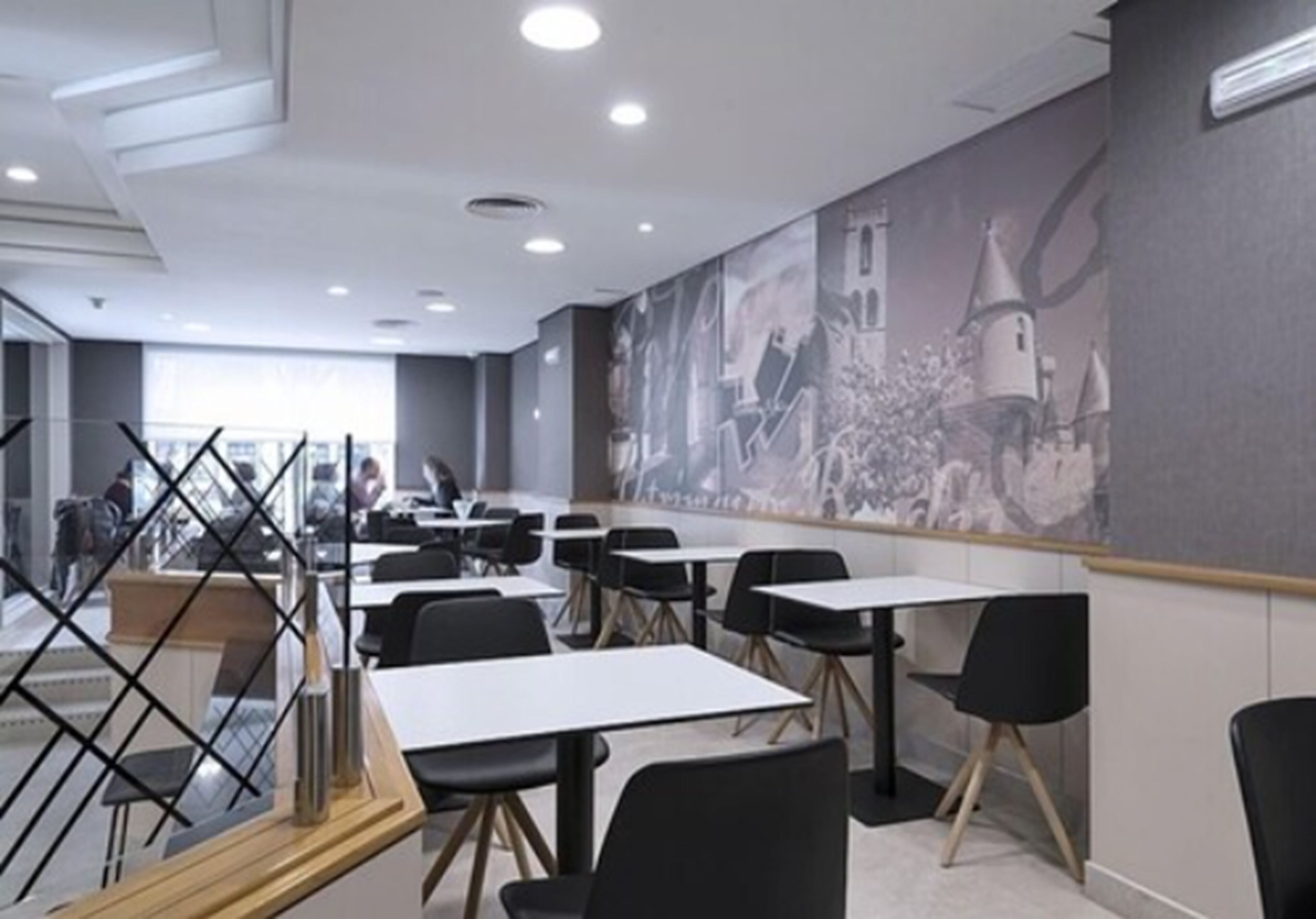 A modern dining area with tables and chairs, a large mural on the wall, and a view of the city through large windows.