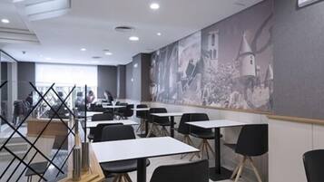 A modern dining area with tables and chairs, a large mural on the wall, and a view of the city through large windows.